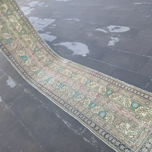 Puede incluir: Una alfombra larga y rectangular con fondo crema y un patrón geométrico colorido. La alfombra tiene flecos en los extremos.