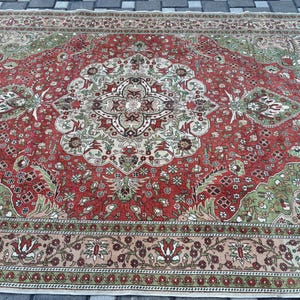 May include: A large, rectangular rug with an intricate, traditional design. The rug features a central medallion and corner designs in shades of red, green, beige, and cream. The border is a floral pattern in similar colors. The rug is likely made of wool.