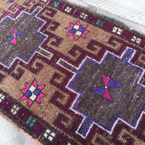 May include: A brown, pink, blue and white patterned rug with a geometric design. The rug has a fringed border.