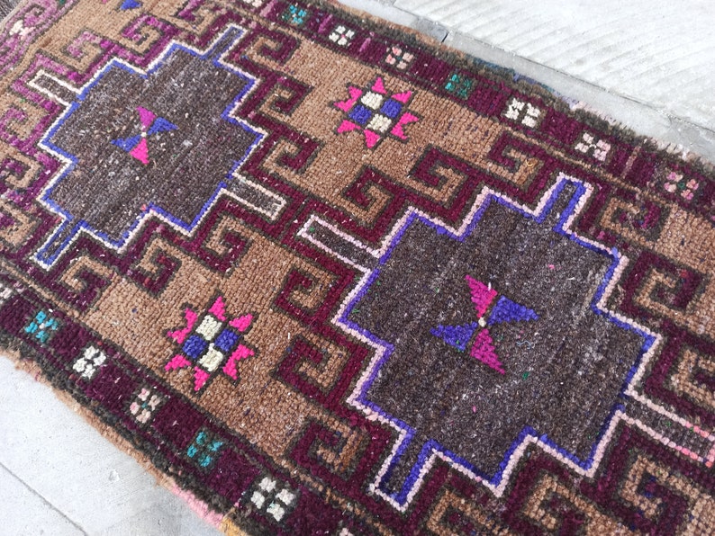 May include: A brown, pink, blue and white patterned rug with a geometric design. The rug has a fringed border.