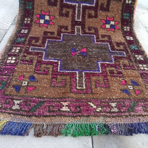 May include: A brown, pink and blue patterned rug with a geometric design. The rug has a fringe border and is made of wool.