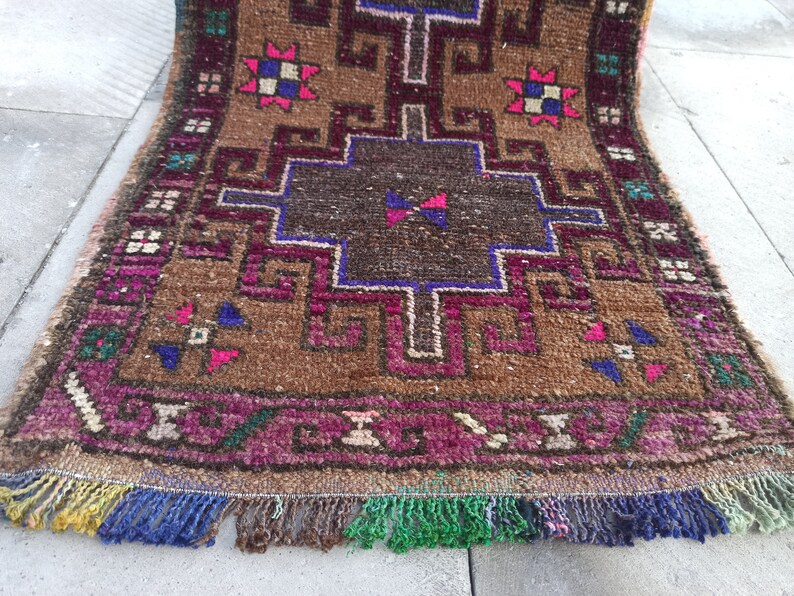 May include: A brown, pink and blue patterned rug with a geometric design. The rug has a fringe border and is made of wool.