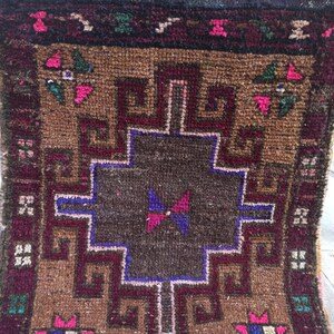 May include: A brown and burgundy rug with a geometric pattern in the centre. The rug has a fringed border and is made of wool.