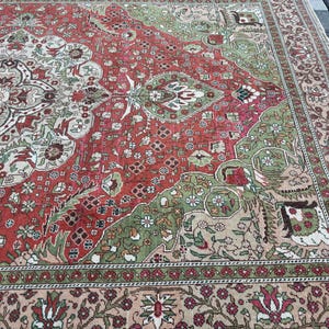 May include: An antique, rectangular rug with a detailed floral pattern. The rug features a central design in red, green, and cream colors, with a border in a similar color palette. The rug's design is intricate and appears to be hand-knotted.