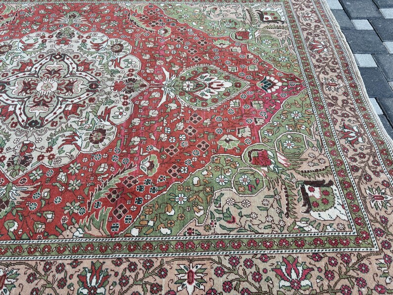 May include: An antique, rectangular rug with a detailed floral pattern. The rug features a central design in red, green, and cream colors, with a border in a similar color palette. The rug's design is intricate and appears to be hand-knotted.
