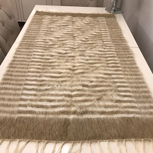 Puede incluir: Una alfombra rayada beige y blanca con un borde de flecos. La alfombra tiene un patrón tejido con un diseño geométrico sutil.