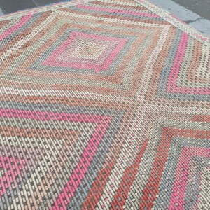 May include: A vintage rug with a geometric pattern in shades of pink, gray, and brown. The rug has a diamond shape in the center and a border with a repeating pattern.
