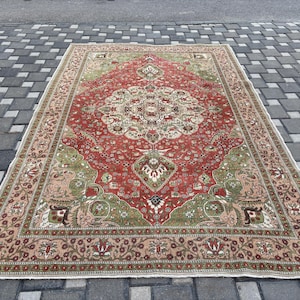 May include: A rectangular, vintage-style rug with a central medallion design. The rug features a red field with green and beige accents, and a detailed border. The rug is placed on a gray brick surface.