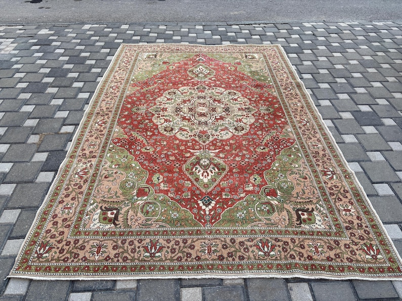 May include: A rectangular, vintage-style rug with a central medallion design. The rug features a red field with green and beige accents, and a detailed border. The rug is placed on a gray brick surface.
