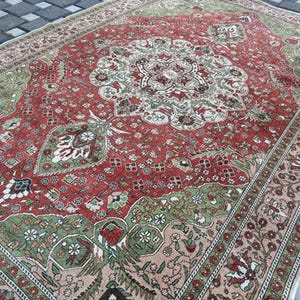 May include: A rectangular, vintage-style rug with an intricate floral pattern. The rug features a central medallion design in shades of red, green, and cream, surrounded by a border with floral motifs. The rug's color palette includes red, green, cream, and beige.