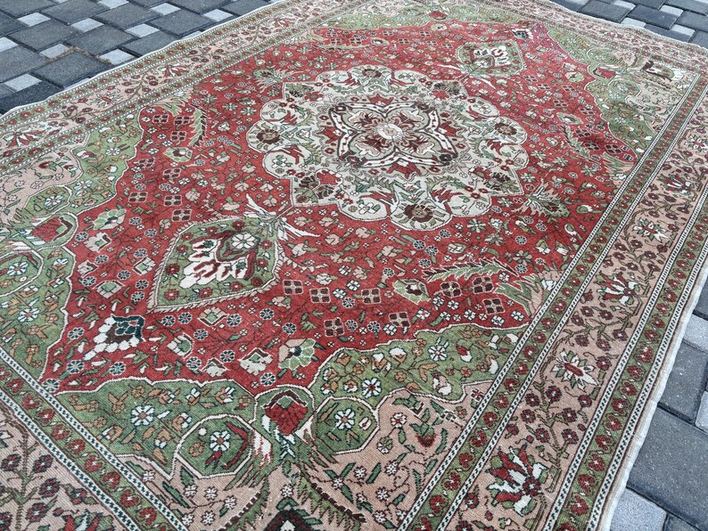 May include: A rectangular, vintage-style rug with an intricate floral pattern. The rug features a central medallion design in shades of red, green, and cream, surrounded by a border with floral motifs. The rug's color palette includes red, green, cream, and beige.