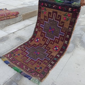 May include: A brown and burgundy rug with a geometric pattern in shades of blue, red, and white. The rug has fringe on the edges.