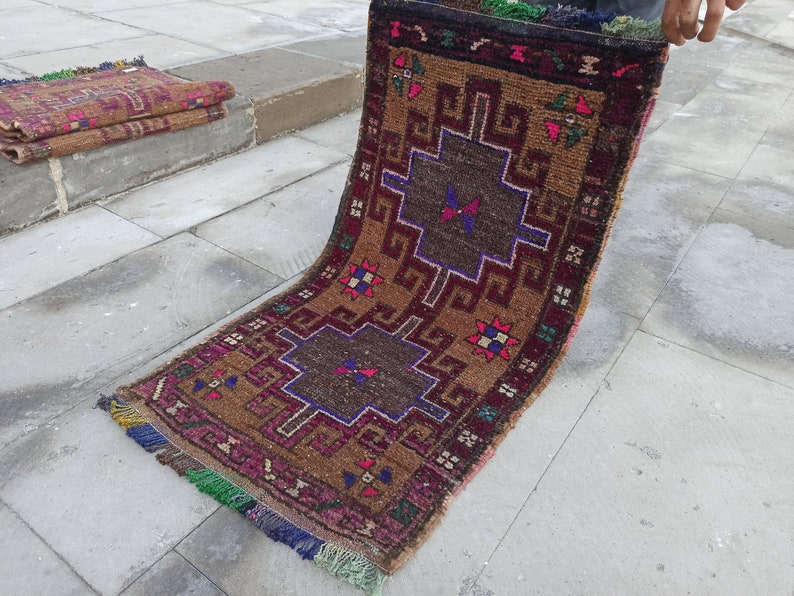 May include: A brown and burgundy rug with a geometric pattern in shades of blue, red, and white. The rug has fringe on the edges.