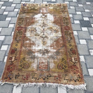 May include: A rectangular, distressed rug with a central medallion design. The rug has a warm colour palette of brown, beige, and red, with intricate floral and geometric patterns. Fringed edges add texture to this vintage-style floor covering.
