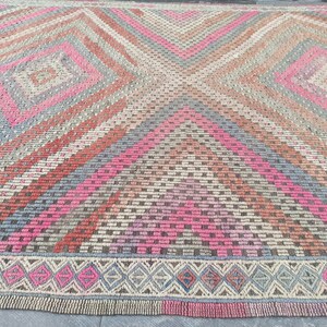 May include: A vintage rug with a geometric pattern in shades of pink, red, gray, and brown. The rug has a diamond pattern with a border of smaller diamonds.