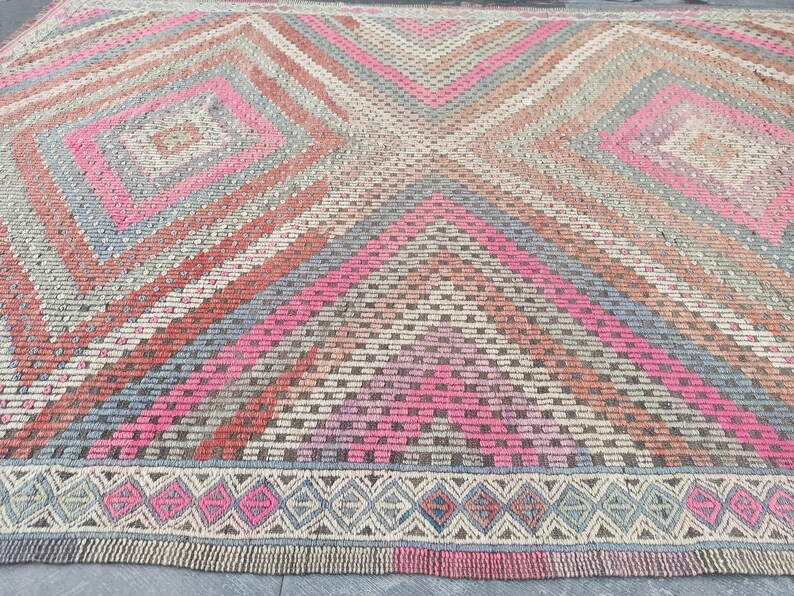 May include: A vintage rug with a geometric pattern in shades of pink, red, gray, and brown. The rug has a diamond pattern with a border of smaller diamonds.