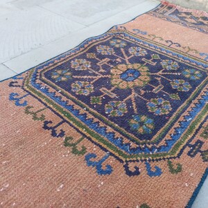 May include: A brown and blue patterned rug with a geometric design. The rug has a fringe border and is made of woven fabric.