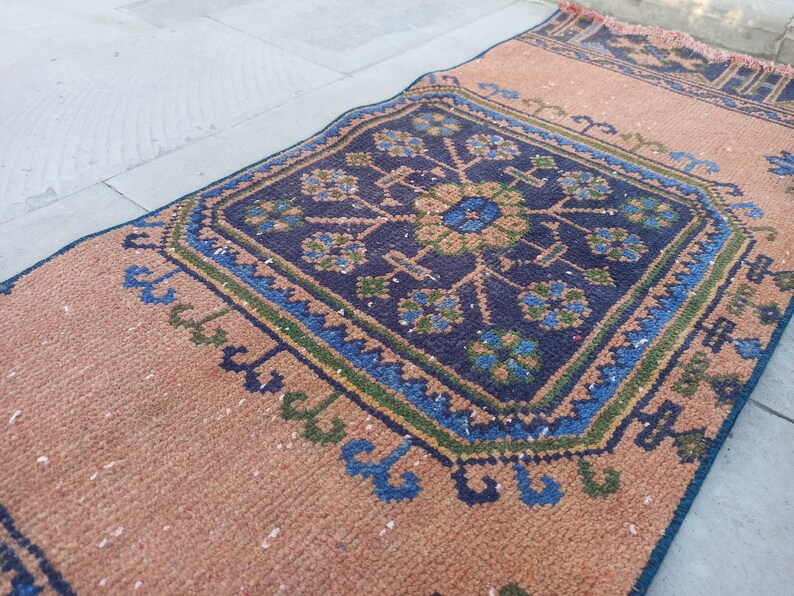 May include: A brown and blue patterned rug with a geometric design. The rug has a fringe border and is made of woven fabric.