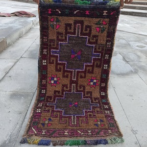 May include: A vintage Turkish rug with a geometric pattern in shades of brown, red, pink, blue, and green. The rug has a fringed border and is folded in half.