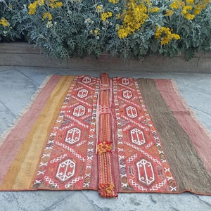 Puede incluir: Una alfombra roja, naranja y marrón con estampado y flecos en los bordes. La alfombra tiene un diseño geométrico con detalles blancos.