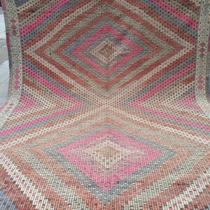 May include: A pink, gray, and brown patterned rug with a diamond shape in the center. The rug is folded in half and the edges are visible.