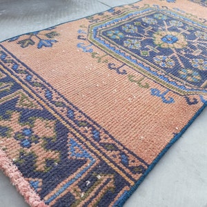 May include: A pink and blue patterned rug with a fringed edge. The rug has a geometric design with a central floral motif.