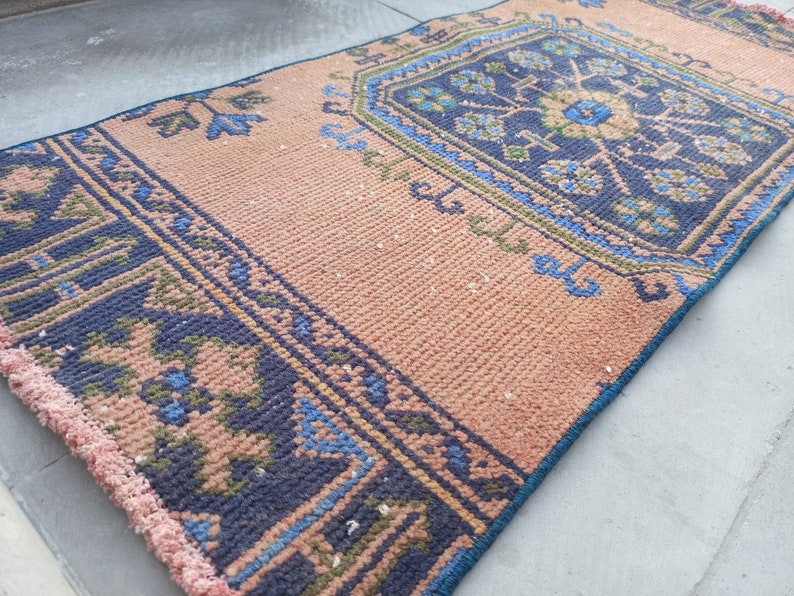 May include: A pink and blue patterned rug with a fringed edge. The rug has a geometric design with a central floral motif.