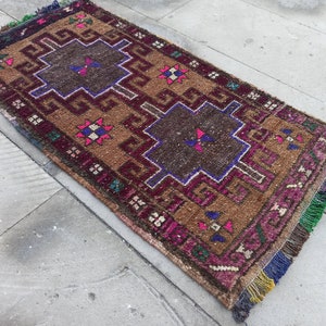 May include: A vintage Turkish rug with a brown background and intricate geometric patterns in shades of pink, blue, and green. The rug has a fringe border.