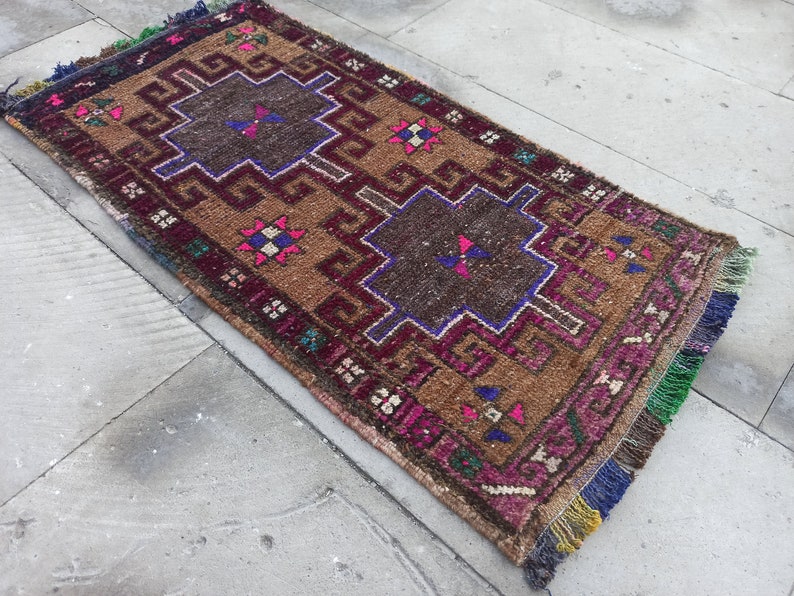 May include: A vintage Turkish rug with a brown background and intricate geometric patterns in shades of pink, blue, and green. The rug has a fringe border.