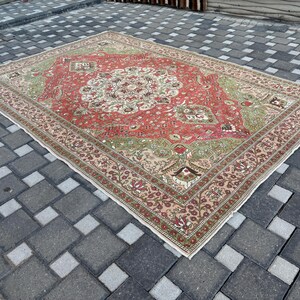 May include: A rectangular, vintage rug with a central medallion design. The rug features a red field with green and cream accents, and a detailed border. The rug is placed on a gray tiled surface.