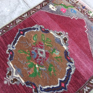 Puede incluir: Una alfombra turca vintage con fondo rojo y un medall&oacute;n central con un dise&ntilde;o floral en tonos marrones, verdes y azules. La alfombra tiene un borde con un patr&oacute;n geom&eacute;trico en tonos grises y blancos.