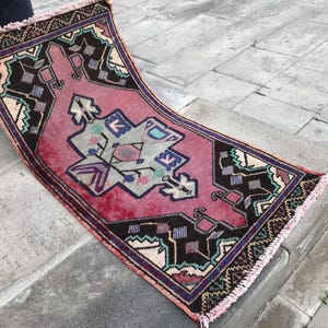 May include: A pink and black patterned rug with a fringed border. The rug features a geometric design with a central diamond shape.
