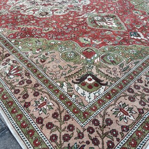 May include: Close-up of a section of a vintage rug with a detailed floral pattern. The rug features a red central field with green and beige accents. The border is a mix of beige, green, and red floral designs.