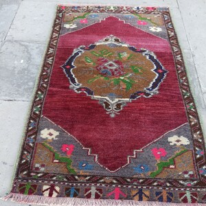 Puede incluir: Una alfombra turca vintage con fondo rojo y un medall&oacute;n central con un dise&ntilde;o floral. La alfombra tiene un borde geom&eacute;trico con una variedad de colores, incluyendo marr&oacute;n, verde, azul y blanco.
