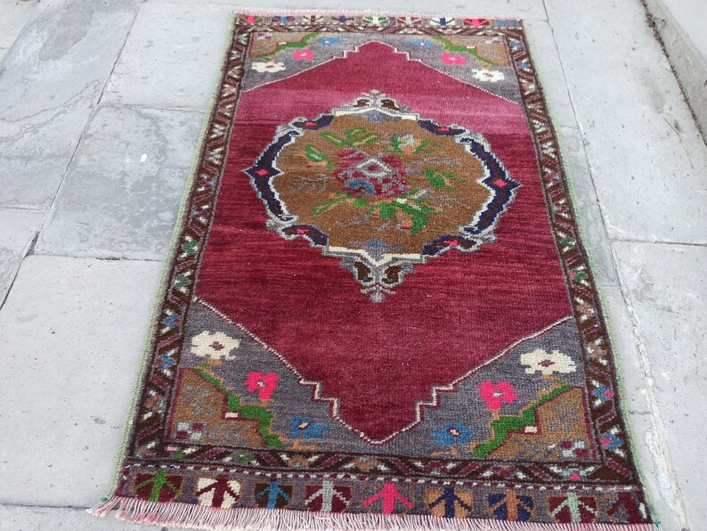 Puede incluir: Una alfombra turca vintage con fondo rojo y un medall&oacute;n central con un dise&ntilde;o floral. La alfombra tiene un borde geom&eacute;trico con una variedad de colores, incluyendo marr&oacute;n, verde, azul y blanco.