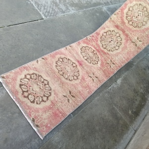 May include: A long, narrow rug with a pink background and brown floral designs. The rug has a fringe on the edges.