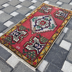 May include: A rectangular area rug featuring a vibrant red background with a central geometric medallion in white, purple, and green. The rug is bordered by a yellow frame with repeating patterns and includes white fringe on the short ends.