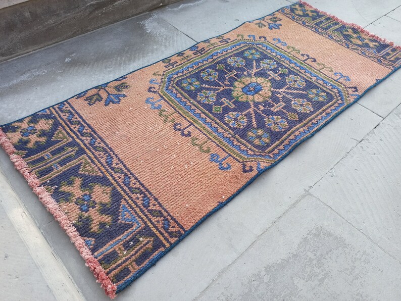 May include: A pink and blue patterned rug with a fringe border. The rug has a central design with a blue background and green and white accents.