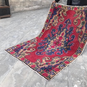 May include: A vintage rug in red, blue and beige with a floral pattern. The rug has a fringed edge and is folded in half.