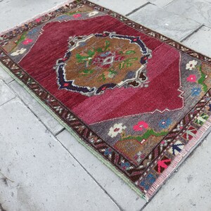 Puede incluir: Una alfombra turca vintage con fondo rojo y un medall&oacute;n central con dise&ntilde;os florales. La alfombra tiene un borde con flecos y est&aacute; hecha de lana.