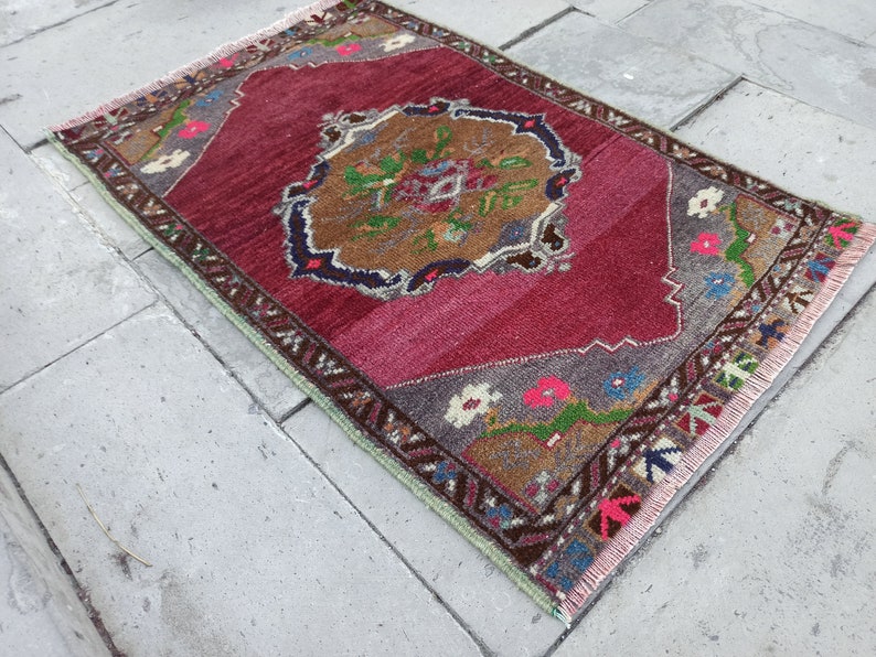 Puede incluir: Una alfombra turca vintage con fondo rojo y un medall&oacute;n central con dise&ntilde;os florales. La alfombra tiene un borde con flecos y est&aacute; hecha de lana.