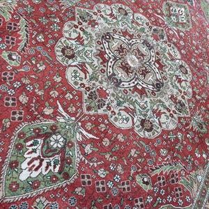 May include: A detailed, antique-style rug with a central medallion design. The rug features a rich red background with intricate patterns in shades of green, beige, and brown. The border has a floral design. The rug is likely made of wool or a similar material.