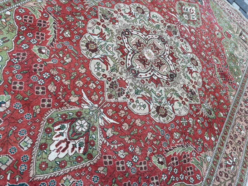May include: A detailed, antique-style rug with a central medallion design. The rug features a rich red background with intricate patterns in shades of green, beige, and brown. The border has a floral design. The rug is likely made of wool or a similar material.
