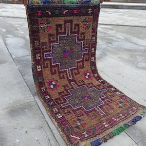 May include: A vintage Turkish rug with a brown, red and blue geometric pattern. The rug has a fringe border and is in good condition.