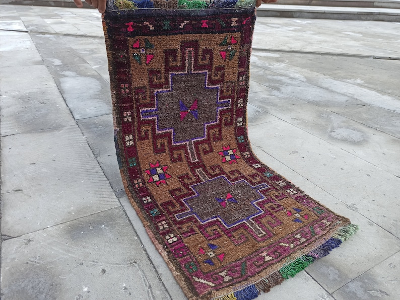 May include: A vintage Turkish rug with a brown, red and blue geometric pattern. The rug has a fringe border and is in good condition.