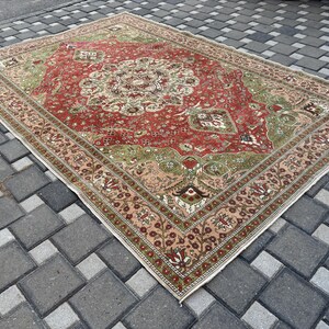 May include: A rectangular, vintage-style rug with a central medallion design. The rug features a red field with green and beige accents, and a detailed border. The rug is placed on a gray brick surface.
