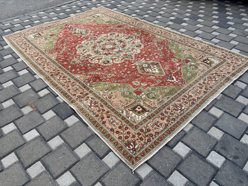 May include: A rectangular, vintage-style rug with a central medallion design. The rug features a red field with green and beige accents, and a detailed border. The rug is placed on a gray brick surface.