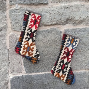 May include: Two colorful Christmas stockings with a traditional Turkish kilim pattern. The stockings are hanging on a stone wall.