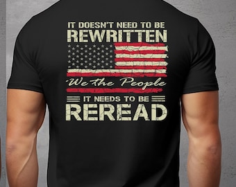 Peut inclure: T-shirt noir avec un drapeau américain vieilli et le texte "We the People" sur le devant. Le dos du t-shirt affiche le texte "It doesn't need to be rewritten, We the People, It needs to be reread".
