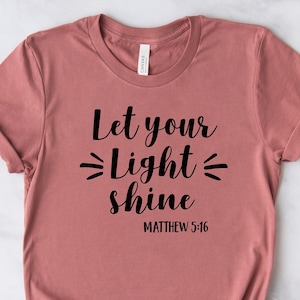 May include: A dusty rose t-shirt with the text "Let your Light shine" and "Matthew 5:16" printed in black.